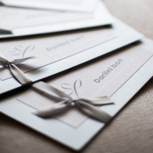 Elegantno oblikovan darilni bon Studio Ping, predstavljen na čistem ozadju; izpostavljen kot univerzalno darilo, ki omogoča izbiro med ličenjem, masažami, oblikovanjem obrvi, depilacijo, nakitom in kozmetiko.