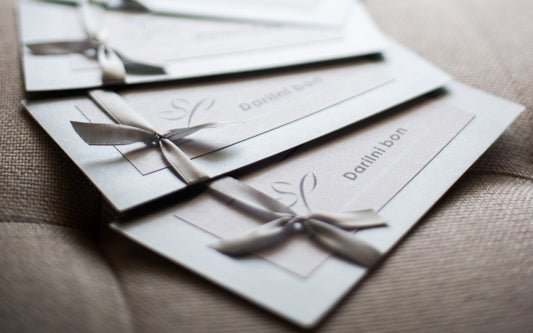 Elegantno oblikovan darilni bon Studio Ping, predstavljen na čistem ozadju; izpostavljen kot univerzalno darilo, ki omogoča izbiro med ličenjem, masažami, oblikovanjem obrvi, depilacijo, nakitom in kozmetiko.